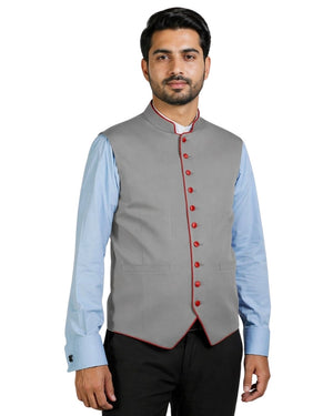 Man wearing a gray vest with red buttons over a light blue shirt on a white background.