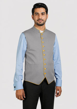 Man wearing a gray vest with yellow buttons over a light blue shirt on a white background
