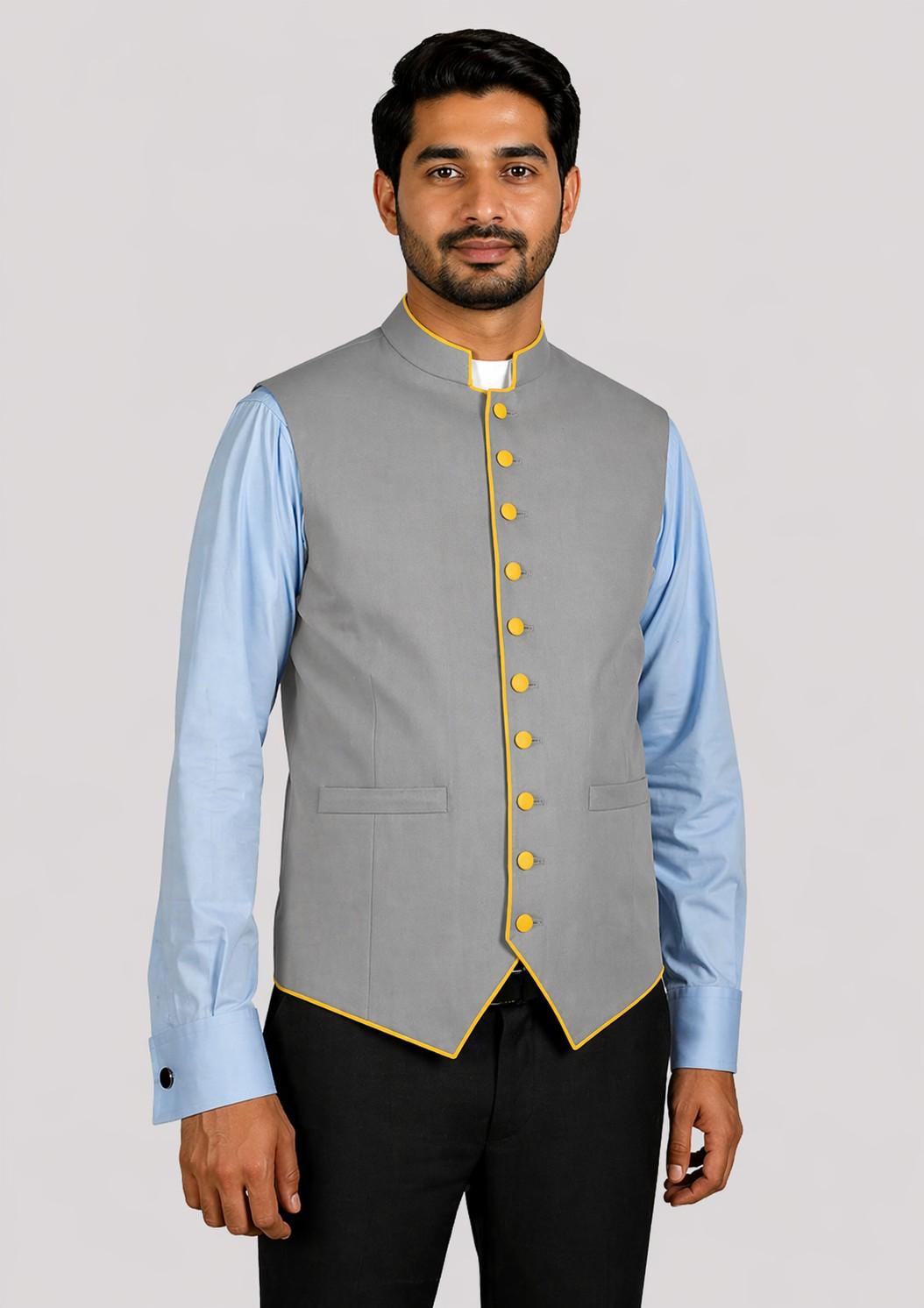 Man wearing a gray vest with yellow buttons over a light blue shirt on a plain background
