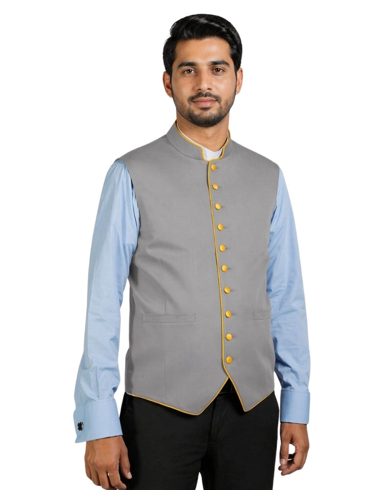 Man wearing a gray vest with yellow buttons over a light blue shirt on a white background.