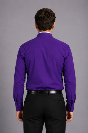 Man wearing a purple shirt with a clerical collar against a gray background