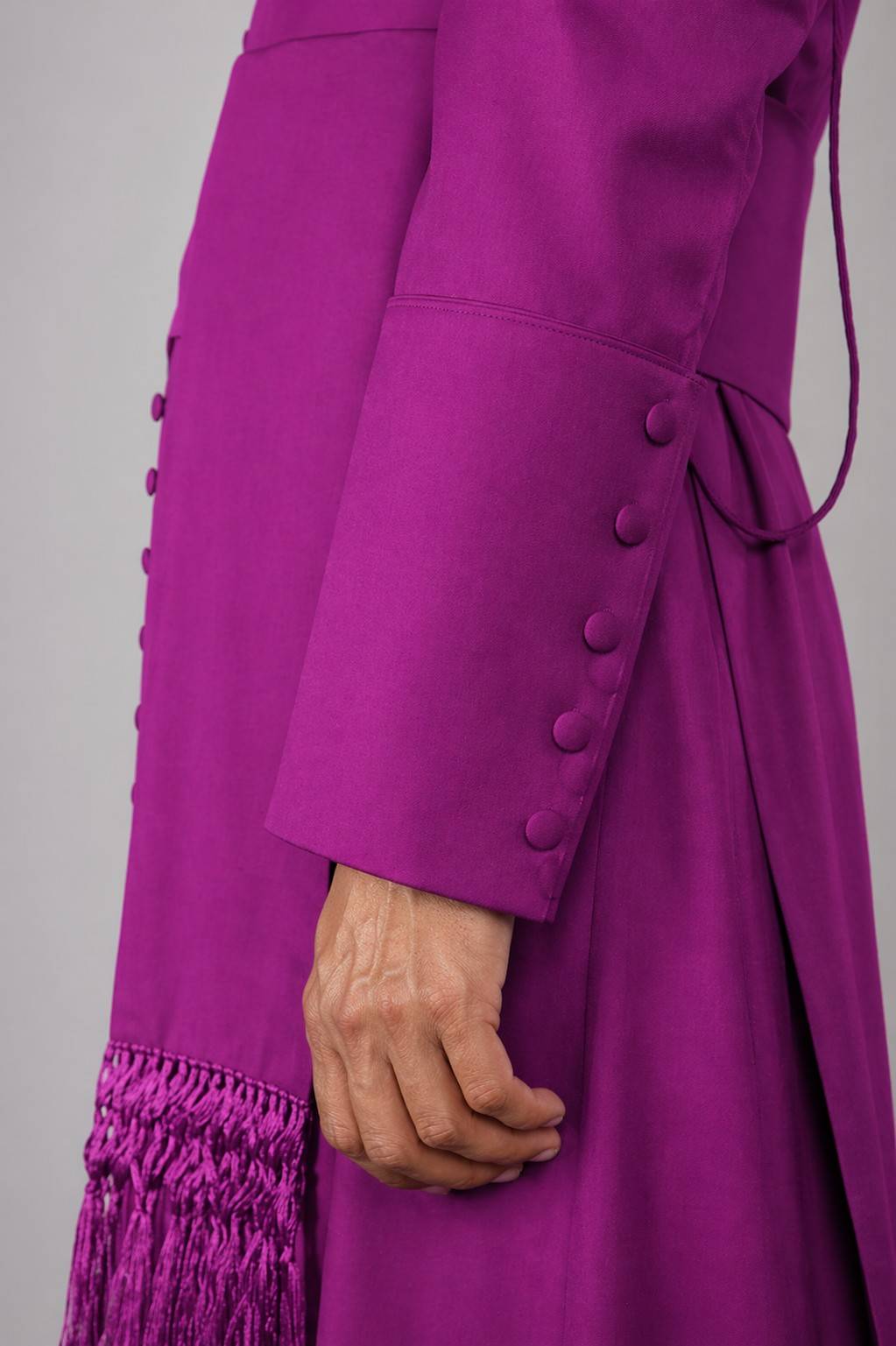 Close-up of a purple coat with buttons and fringes on a gray background