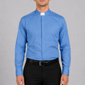Man wearing a blue clerical shirt with a white collar against a gray background