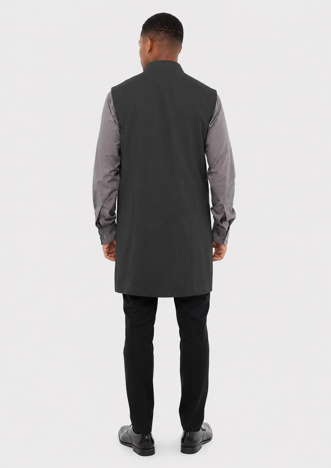 Man wearing a long dark gray vest over a gray shirt with black pants on a white background