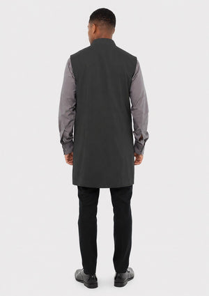 Man wearing a long dark gray vest over a gray shirt with black pants on a white background