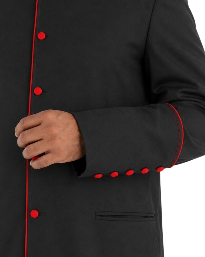 Close-up of a black cassock with bright red piping and red buttons, shown on a person whose hand is visible near the front closure.