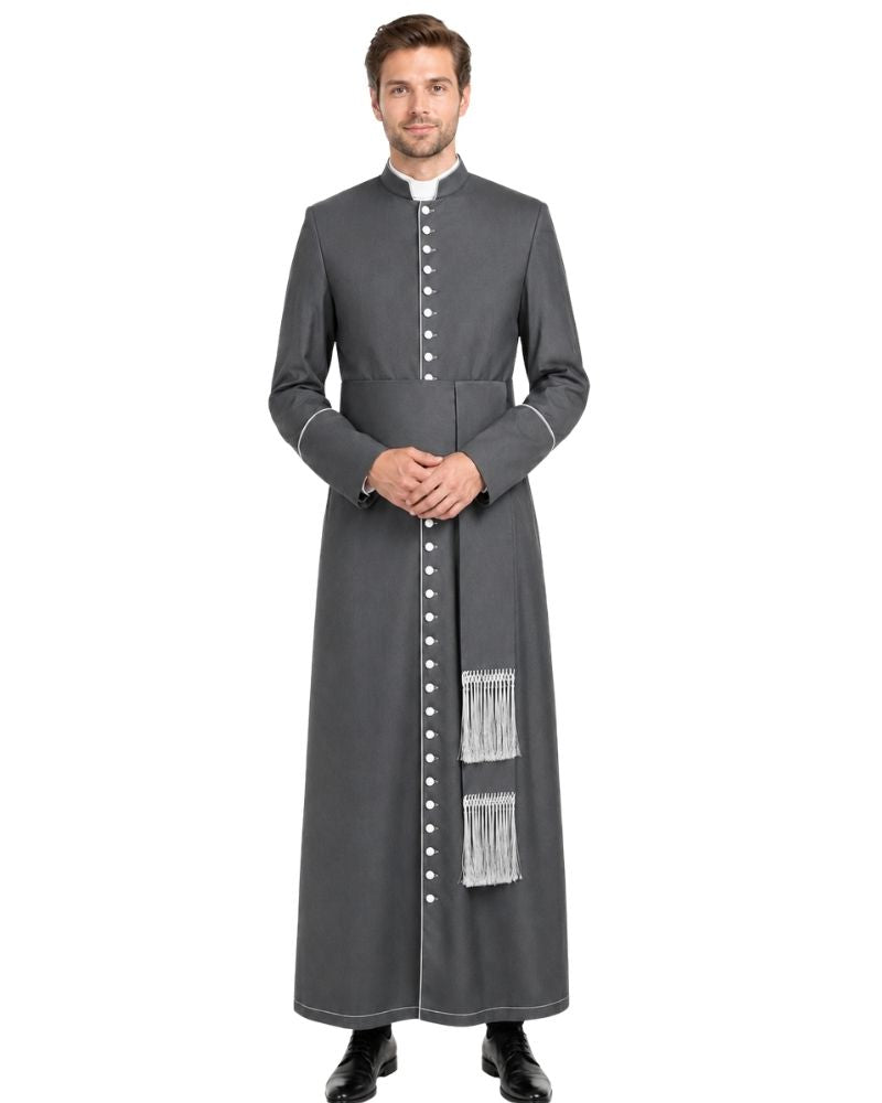 A man modeling a long dark gray clergy cassock with white trim, a white collar, and silver-toned buttons, standing against a plain white background.