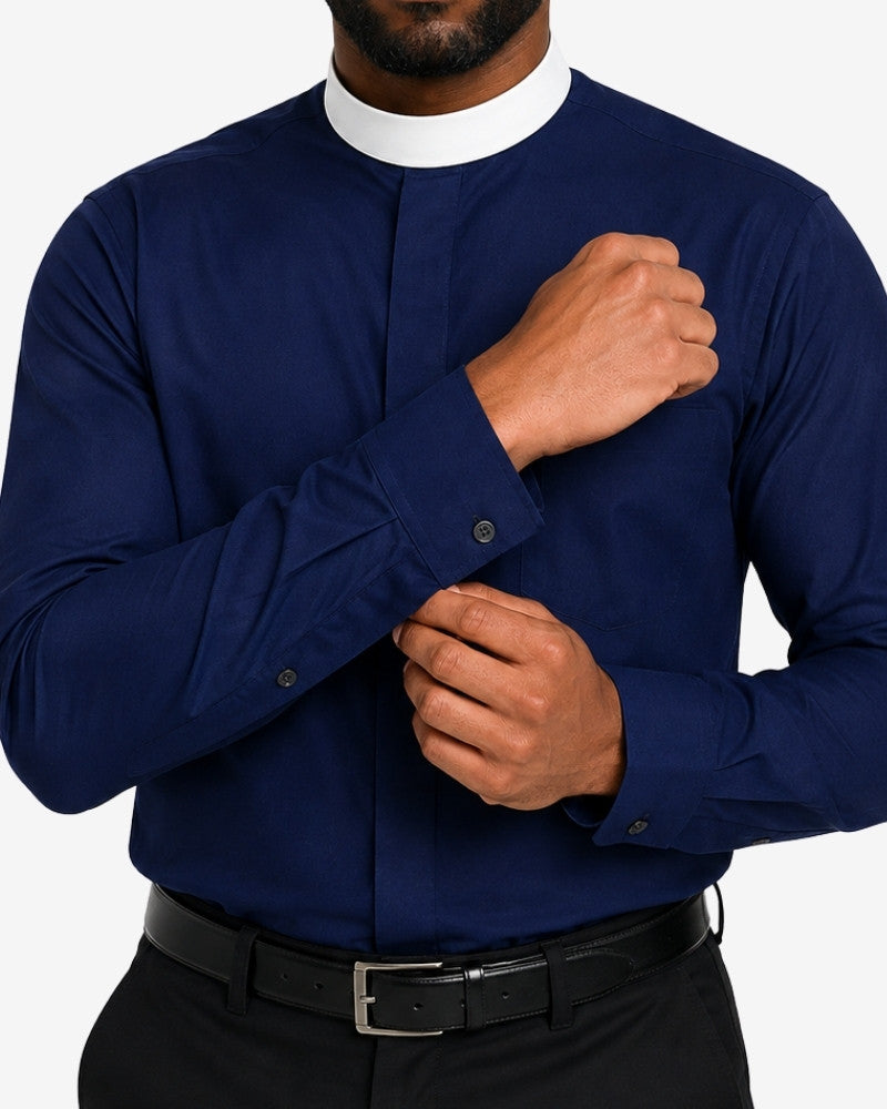A man wearing a navy blue long-sleeve clerical shirt with a white collar, paired with a black belt and dark trousers, adjusting the cuff of the shirt.