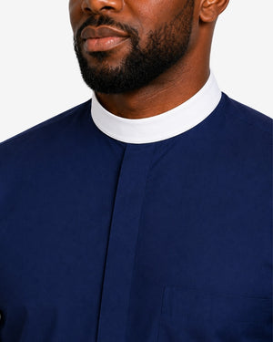 Close-up of a man wearing a navy blue clerical shirt with a contrasting white mock neck collar, shown against a plain light background.