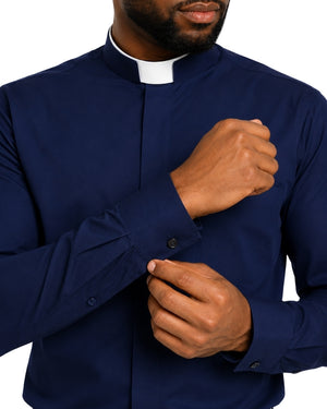 A close-up of a man wearing a navy blue long-sleeve clerical shirt with a white clerical collar, adjusting his cuff against a plain white background.