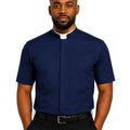 A man wearing a navy blue short-sleeve clerical shirt with a white collar tab, paired with black trousers and a black belt, against a plain white background.