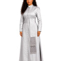 A woman modeling a long-sleeved silver satin cassock with a high collar, buttoned front, a wide waist sash, and a decorative silver fringe panel on the skirt, set against a plain white background.