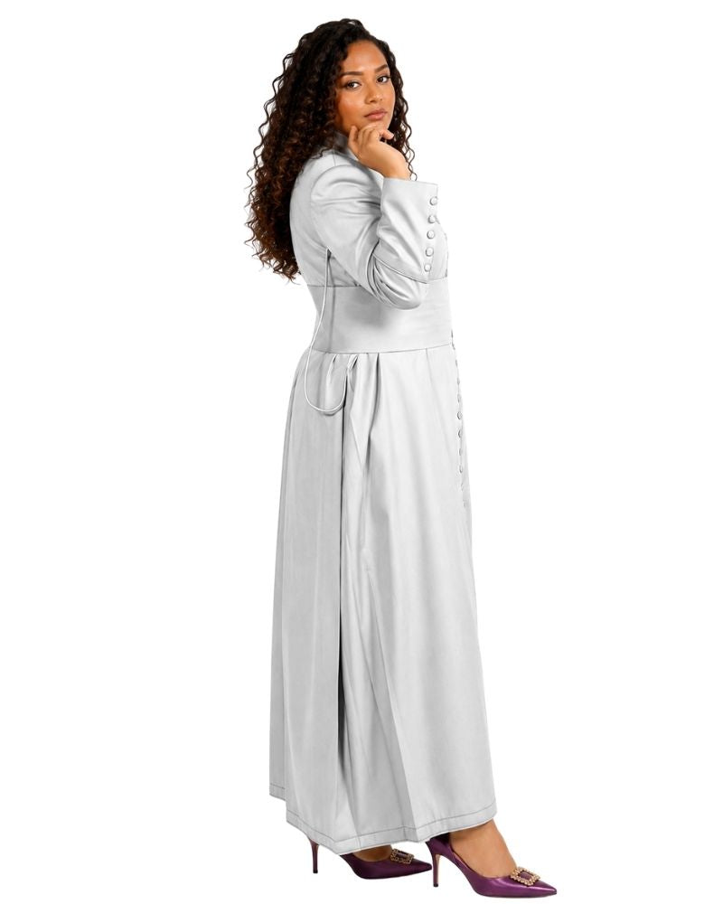 A woman modeling a long-sleeved, floor-length white cassock with button details down the front and a matching belt, paired with purple high heels, against a plain white background.