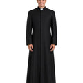 A man wearing a long black clerical robe with a high collar and a white clerical collar, standing against a plain white background.
