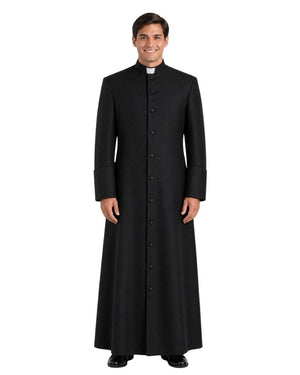 A man wearing a long black clerical robe with a high collar and a white clerical collar, standing against a plain white background.