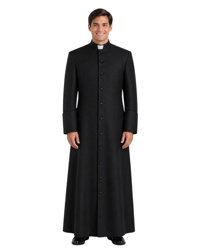 A man wearing a long black clerical robe with a high collar and a white clerical collar, standing against a plain white background.