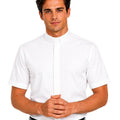 A man wearing a white short-sleeve clerical shirt with a unique high stand-up collar, paired with black trousers and a black belt, against a plain white background.