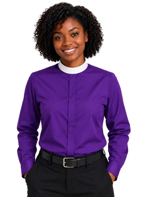 A smiling woman with curly black hair wearing a purple long-sleeve clerical shirt with a white mock neck collar, paired with black trousers and a black belt, against a plain white background.