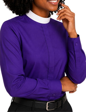 A woman wearing a long-sleeve purple clerical shirt with a white mock neck collar, paired with a black belt and dark trousers, shown against a plain white background.