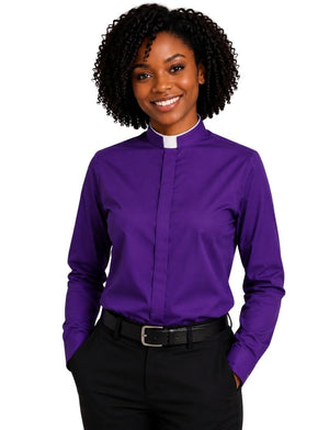A smiling woman with curly black hair wearing a purple long-sleeve clerical shirt with a white collar, paired with black trousers and a black belt, against a plain white background.