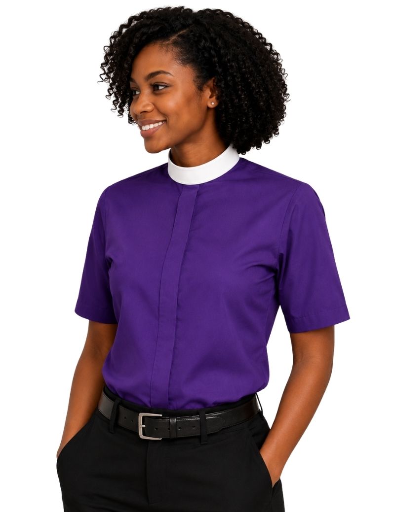 A woman wearing a purple short-sleeve clerical shirt with a white mock neck collar, paired with black trousers and a black belt, against a plain white background.