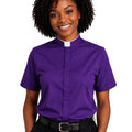 A woman wearing a purple short-sleeve clerical shirt with a white collar, standing against a plain white background.