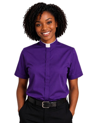 A woman wearing a purple short-sleeve clerical shirt with a white collar, standing against a plain white background.