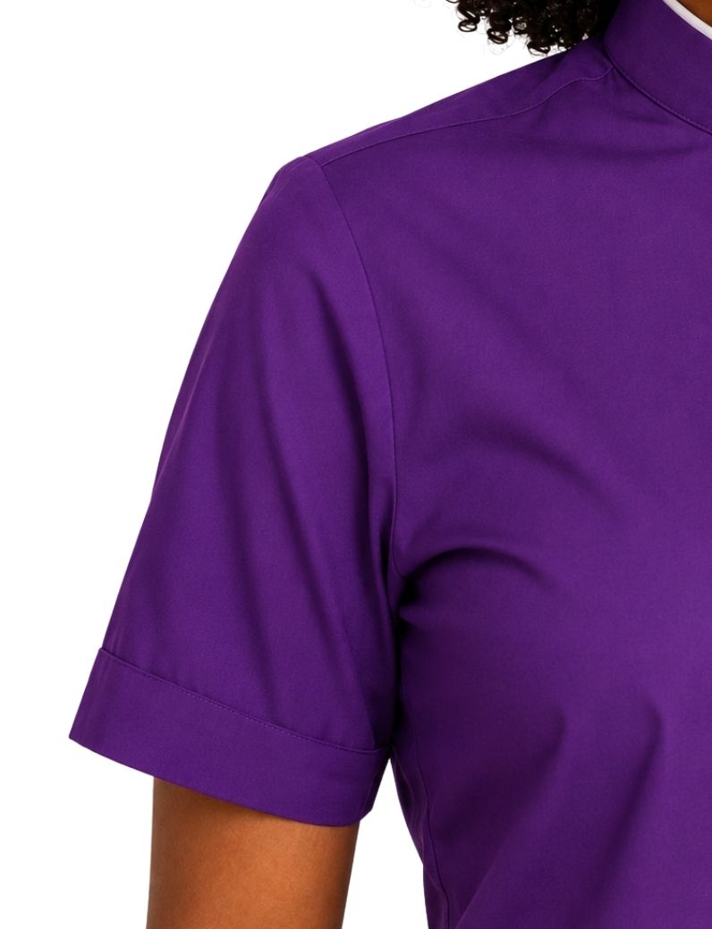 Close-up of a woman wearing a solid purple short-sleeve clerical shirt, showing the chest, shoulder, and sleeve against a plain white background.
