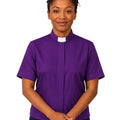 A woman wearing a purple short-sleeve clerical shirt with a white collar, standing against a plain white background.