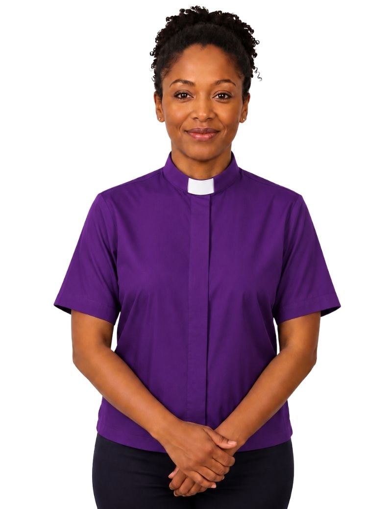 A woman wearing a purple short-sleeve clerical shirt with a white collar, standing against a plain white background.