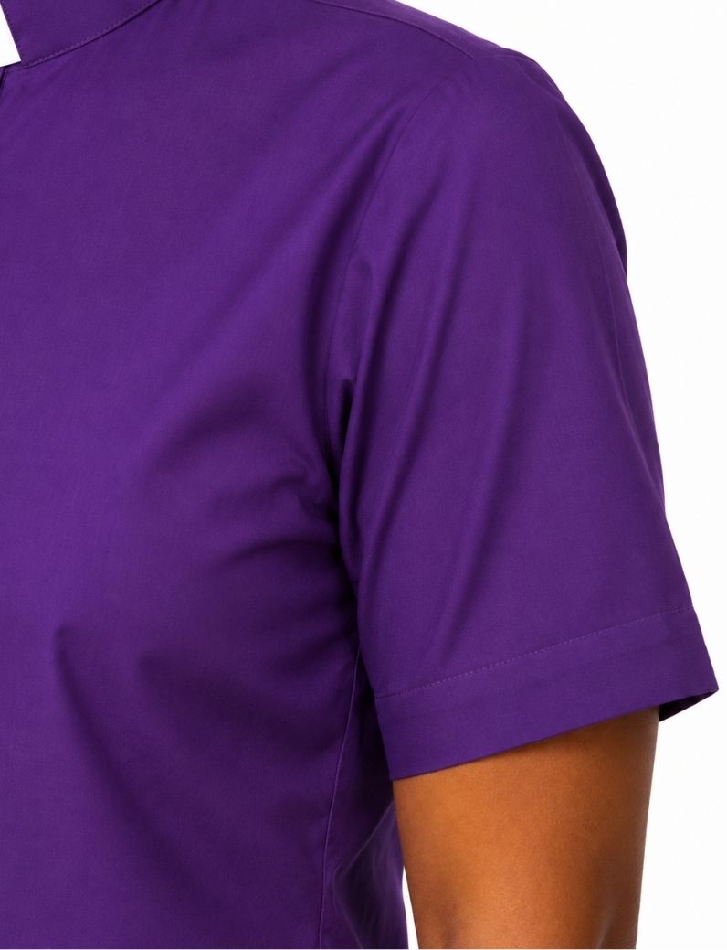 Close-up of a woman wearing a solid purple short-sleeve clerical shirt, showing the chest, shoulder, and sleeve against a plain white background.