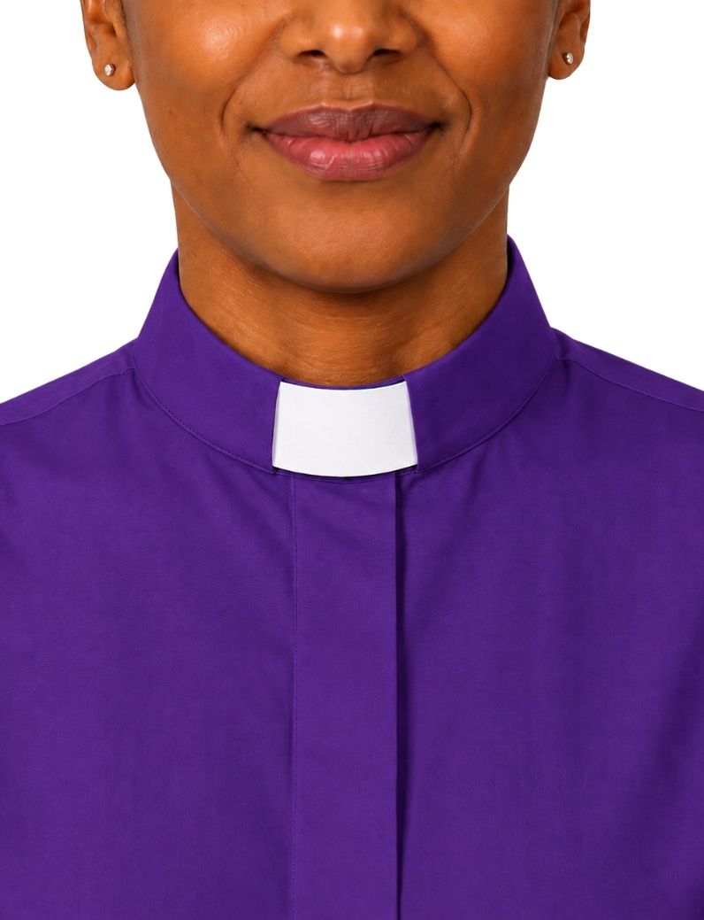 A close-up of a woman wearing a purple clerical shirt with a white collar tab, shown against a plain white background.