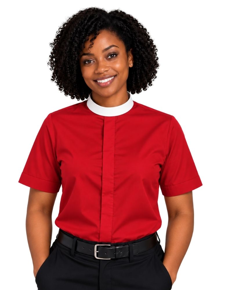 A smiling woman with curly black hair wearing a bright red short-sleeve clerical shirt with a white mock neck collar, paired with black trousers and a black belt, against a plain white background.