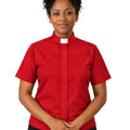 A woman wearing a short-sleeve red clerical shirt with a white collar, paired with black trousers, standing against a plain white background.