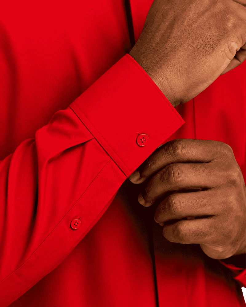 Close-up of a man wearing a bright red long-sleeve clerical shirt, adjusting the cuff with one hand while the other hand rests near the pocket.