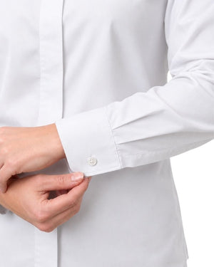 Close-up of a women hands adjusting the cuff of a white long-sleeve clerical shirt, showing a single white button on a clean white background.