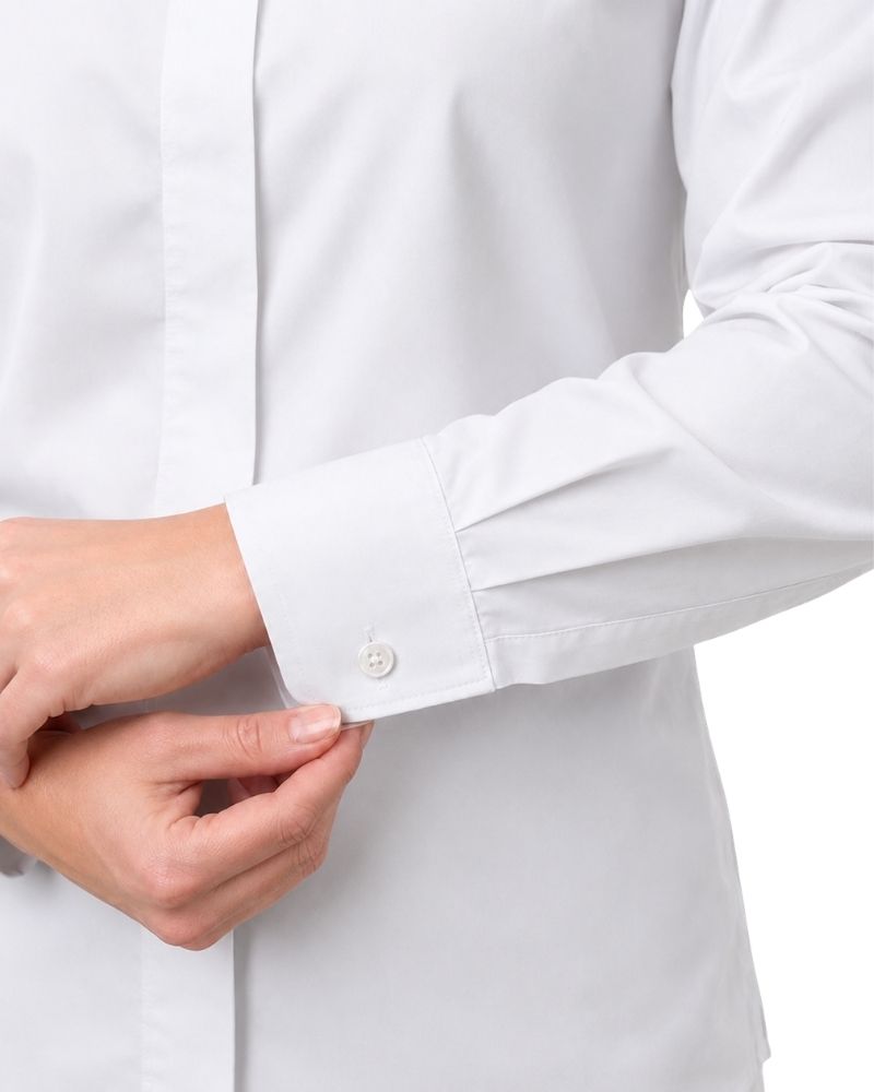Close-up of a women hands adjusting the cuff of a white long-sleeve clerical shirt, showing a single white button on a clean white background.