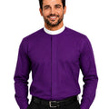 A smiling man wearing a purple long-sleeve clerical shirt with a white mock neck collar, paired with black trousers and a black belt, against a plain white background.