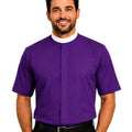 A man viewed from the front wearing a solid purple short-sleeve clerical shirt tucked into black trousers, against a plain white background.