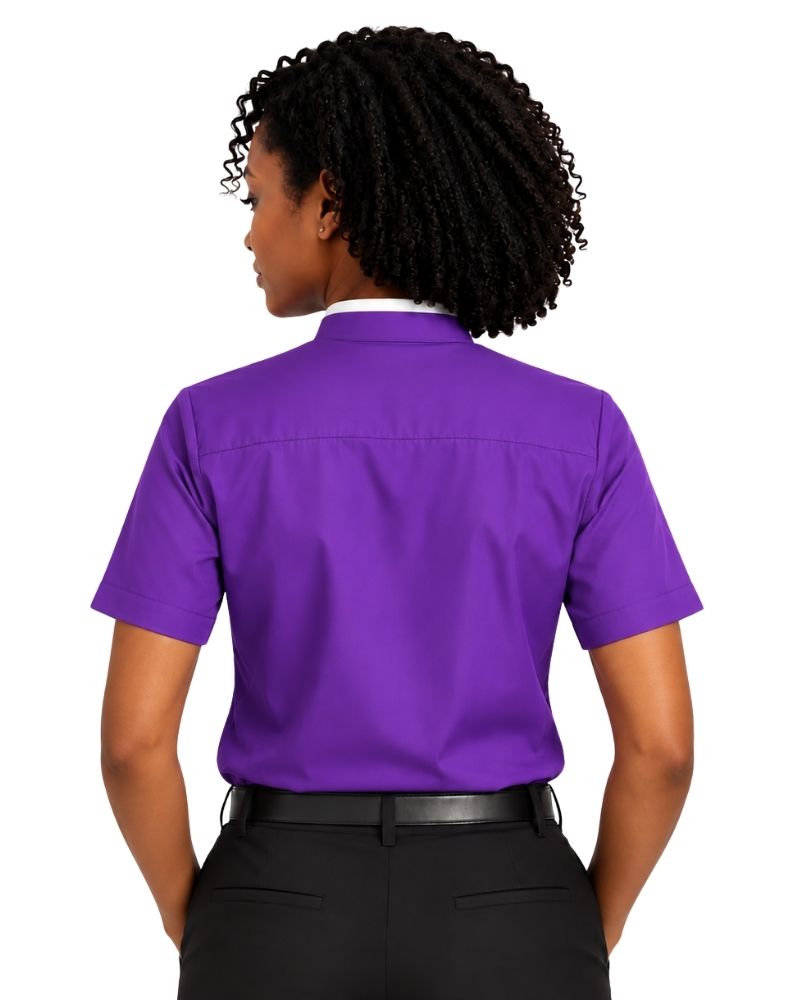 A woman shown from the back wearing a short-sleeve purple clerical shirt tucked into black pants, against a plain white background.