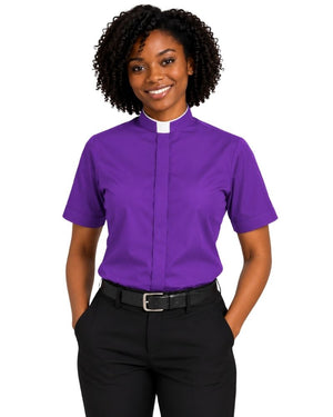 A smiling woman with curly black hair wearing a purple short-sleeve clerical shirt with a white collar tab, paired with black trousers and a black belt, against a plain white background.
