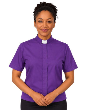 A woman wearing a purple short-sleeve clerical shirt with a white collar, standing against a plain white background.