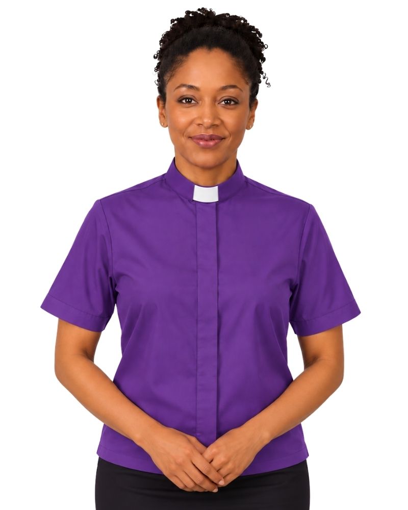 A woman wearing a purple short-sleeve clerical shirt with a white collar, standing against a plain white background.