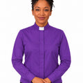 A woman wearing a purple long-sleeve clerical shirt with a white collar, standing against a plain white background.