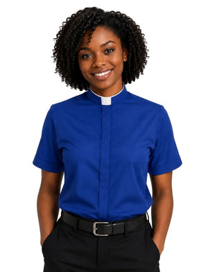 A smiling woman with curly black hair wearing a royal blue short-sleeve clerical shirt with a white collar, paired with black trousers and a black belt, against a plain white background.