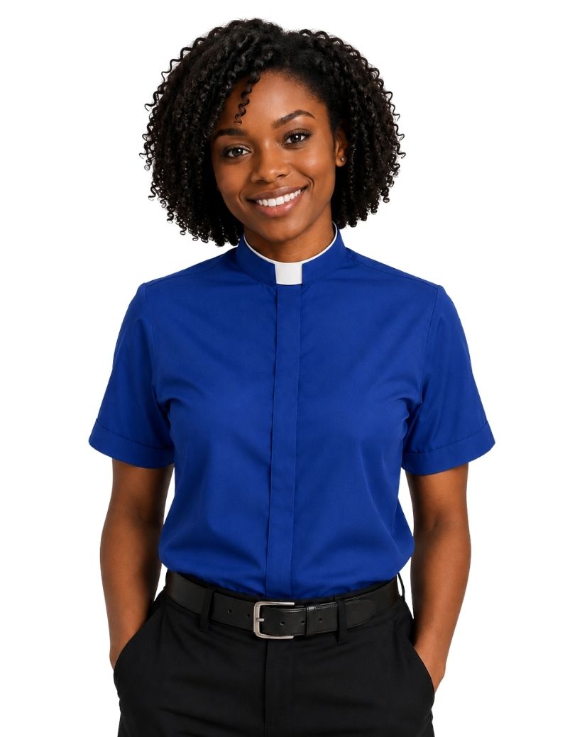 A smiling woman with curly black hair wearing a royal blue short-sleeve clerical shirt with a white collar, paired with black trousers and a black belt, against a plain white background.