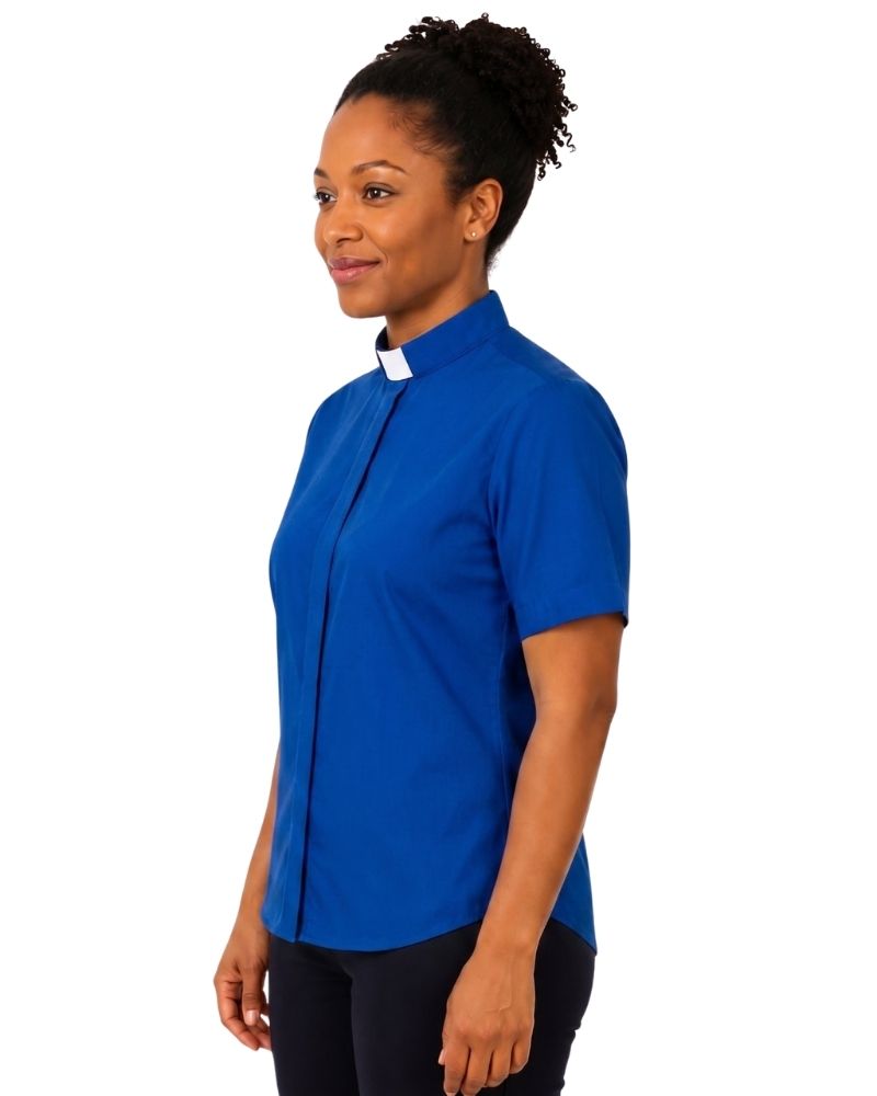 A woman wearing a royal blue short-sleeve clerical shirt with a white collar, standing against a plain white background.