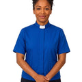 A woman wearing a royal blue short-sleeve clerical shirt with a white collar, standing against a plain white background.