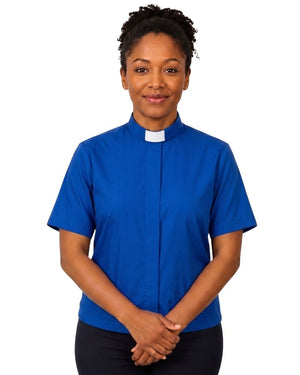 A woman wearing a royal blue short-sleeve clerical shirt with a white collar, standing against a plain white background.