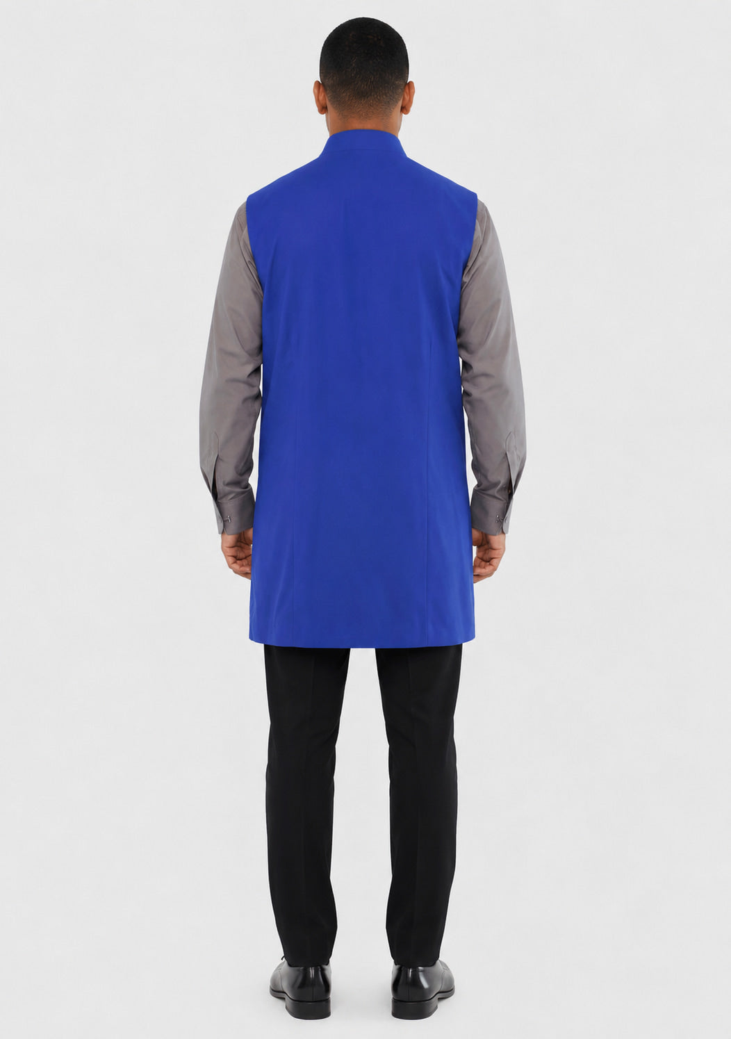 Man wearing a blue vest over a gray shirt with black pants on a white background